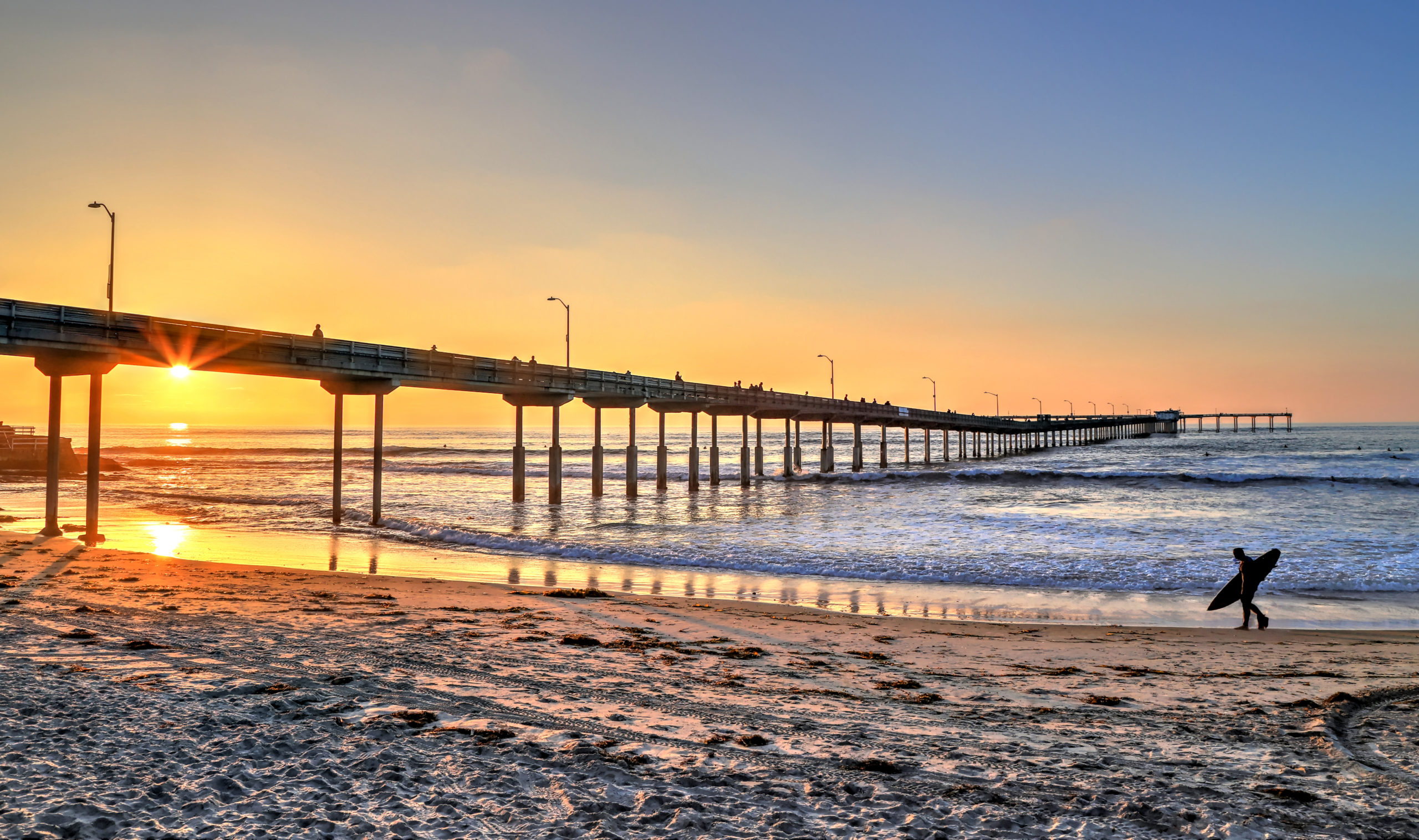 A surfer walks on Ocean Beach near the pier in San Diego, California. A surfer walks on Ocean Beach near the pier in San Diego, California.